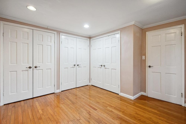 unfurnished bedroom featuring light wood-style flooring, ornamental molding, baseboards, and two closets