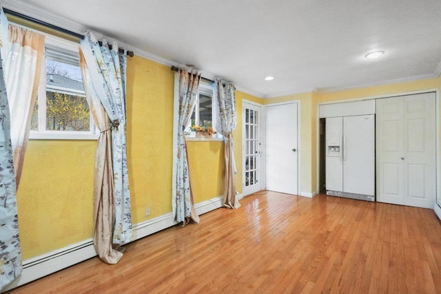 unfurnished bedroom with baseboards, a baseboard heating unit, ornamental molding, white fridge with ice dispenser, and wood finished floors