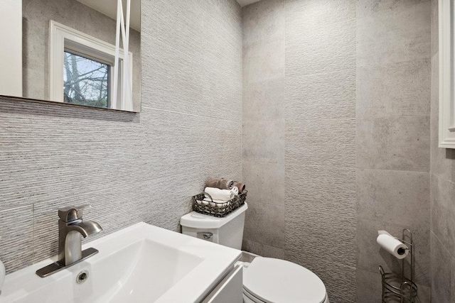 bathroom featuring toilet, tasteful backsplash, vanity, and tile walls