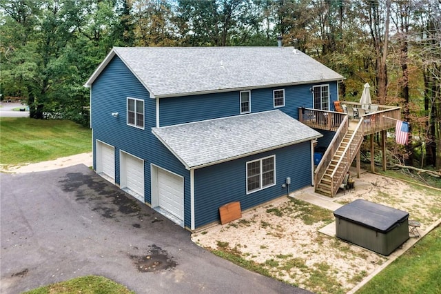 view of front facade with stairway, roof with shingles, a front yard, a wooden deck, and a hot tub