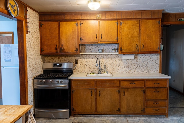 kitchen featuring stainless steel range with gas stovetop, open shelves, a sink, light countertops, and freestanding refrigerator