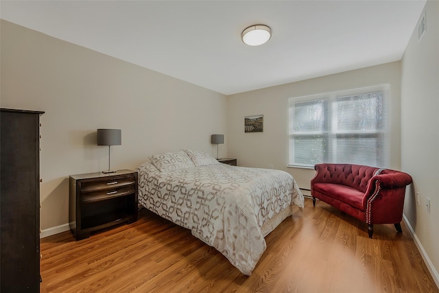 bedroom with visible vents, baseboards, light wood-style flooring, and a baseboard radiator