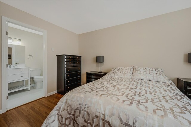 bedroom with connected bathroom, baseboards, and wood finished floors