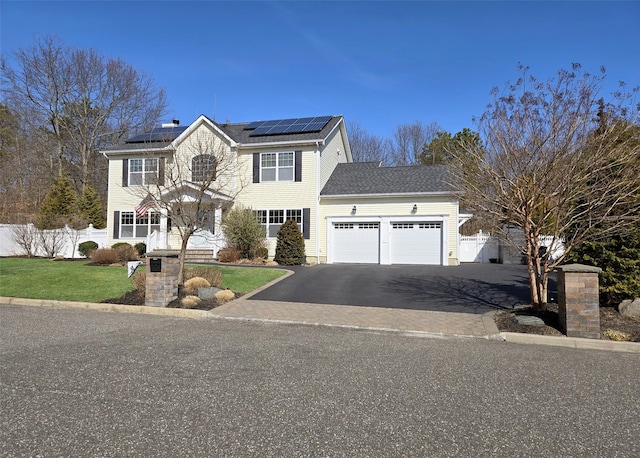 colonial-style house featuring a front yard, fence, driveway, solar panels, and a garage