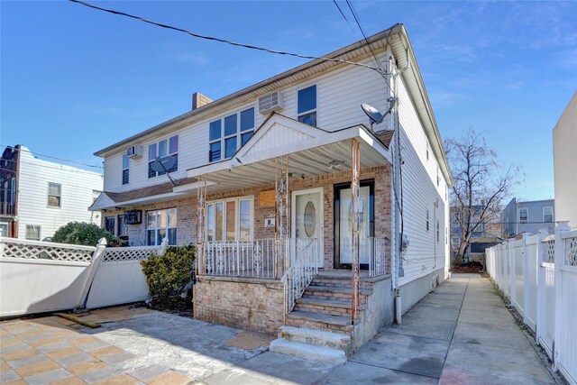 view of front facade featuring an AC wall unit, a porch, fence, and brick siding
