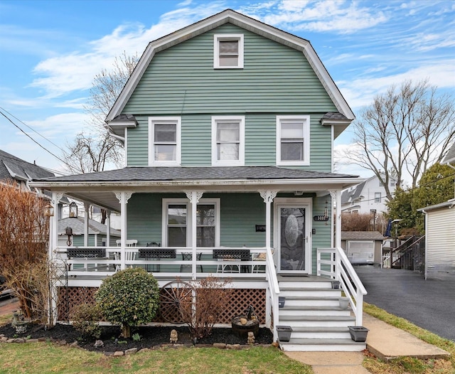 colonial inspired home featuring a garage, covered porch, a gambrel roof, and driveway