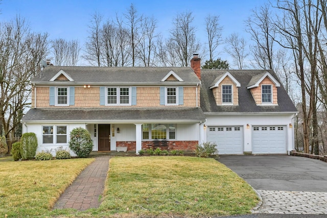 view of front of home with a front lawn, aphalt driveway, covered porch, a chimney, and a garage