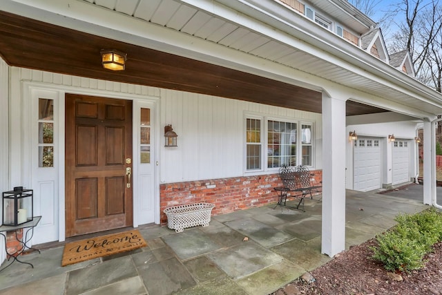 property entrance with a garage, brick siding, and covered porch