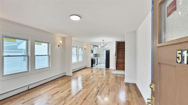 unfurnished living room featuring a baseboard heating unit, light wood-style floors, baseboard heating, a chandelier, and stairs