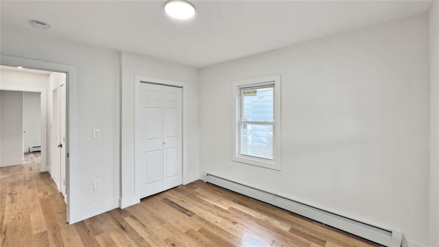 unfurnished bedroom featuring baseboards, a baseboard radiator, light wood-style floors, a closet, and a baseboard heating unit