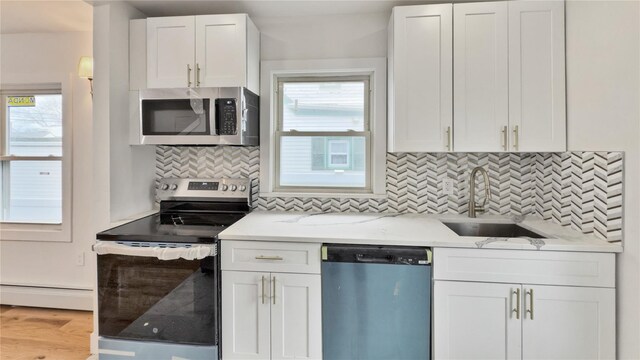 kitchen with a sink, tasteful backsplash, stainless steel appliances, white cabinets, and baseboard heating