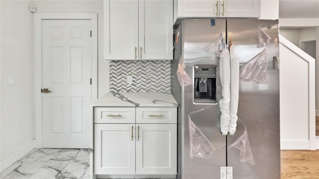kitchen with stainless steel fridge with ice dispenser, light countertops, white cabinetry, marble finish floor, and backsplash