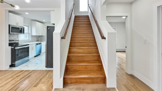 stairs with a wealth of natural light, marble finish floor, baseboards, and a baseboard radiator