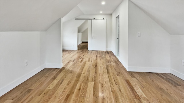 additional living space featuring lofted ceiling, baseboards, light wood-type flooring, and a barn door
