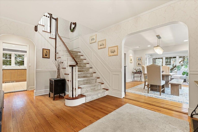 staircase featuring a wainscoted wall, wood finished floors, crown molding, and arched walkways