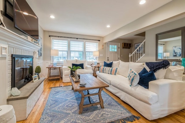 living room featuring a wainscoted wall, a glass covered fireplace, recessed lighting, light wood-style floors, and a decorative wall