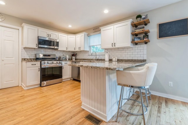 kitchen featuring white cabinetry, appliances with stainless steel finishes, a peninsula, and light wood finished floors