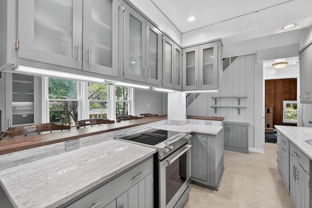 285 Grand St, Croton-On-Hudson, NY 10520 - kitchen featuring stainless steel range with electric cooktop, gray cabinetry, light stone counters, glass insert cabinets, and wood walls