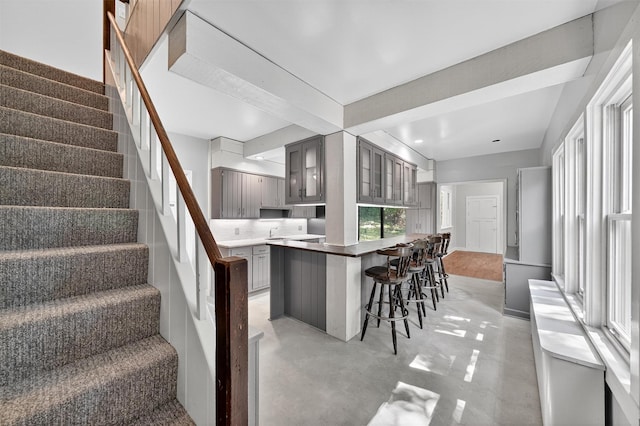 285 Grand St, Croton-On-Hudson, NY 10520 - kitchen with gray cabinetry, finished concrete flooring, a breakfast bar area, glass insert cabinets, and recessed lighting