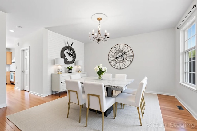 dining area featuring light wood finished floors, a chandelier, baseboards, and visible vents