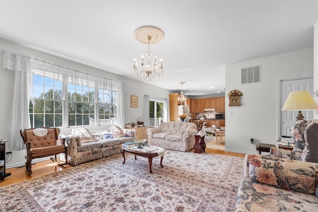 living area with baseboards, an inviting chandelier, visible vents, and light wood-style flooring