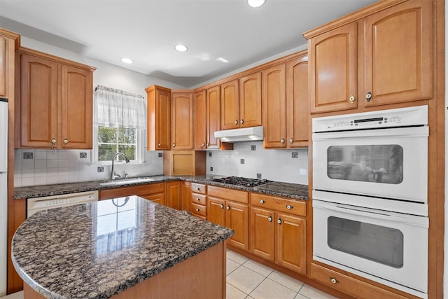 kitchen with a sink, white appliances, dark stone countertops, and tasteful backsplash