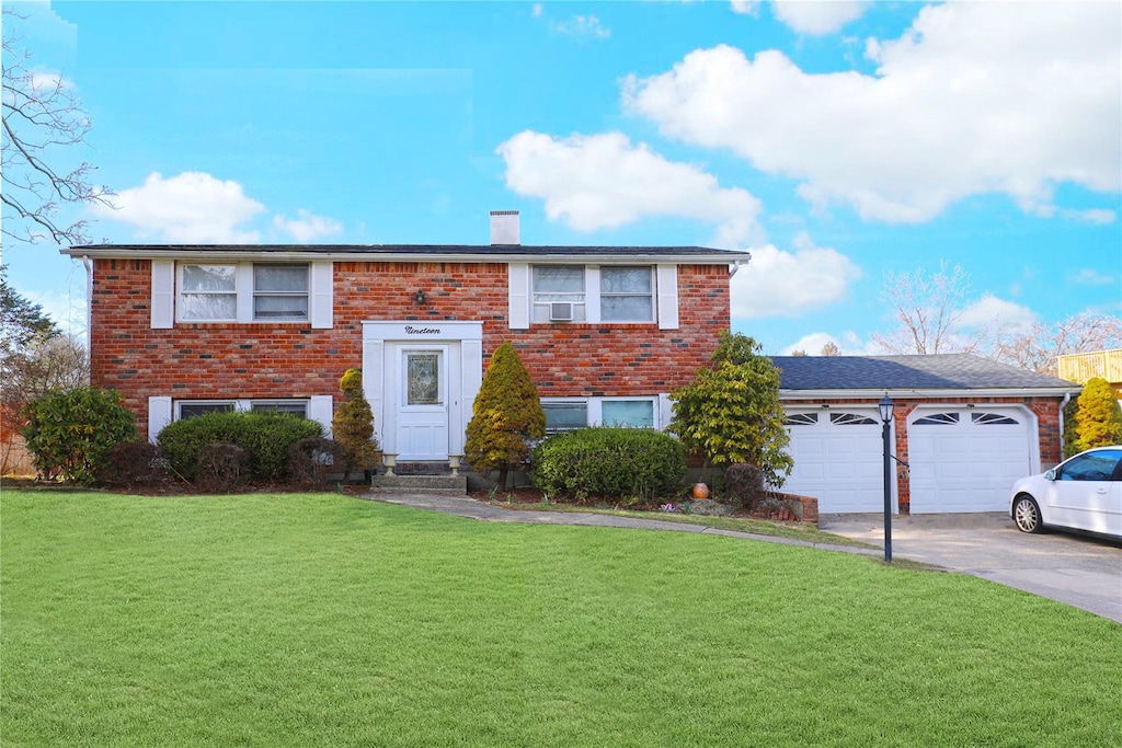 split foyer home featuring brick siding, a front lawn, a chimney, and concrete driveway
