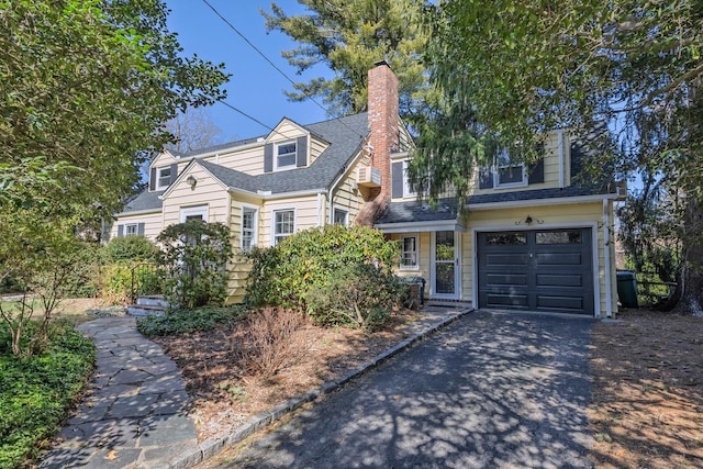 cape cod house featuring a garage, a chimney, and driveway
