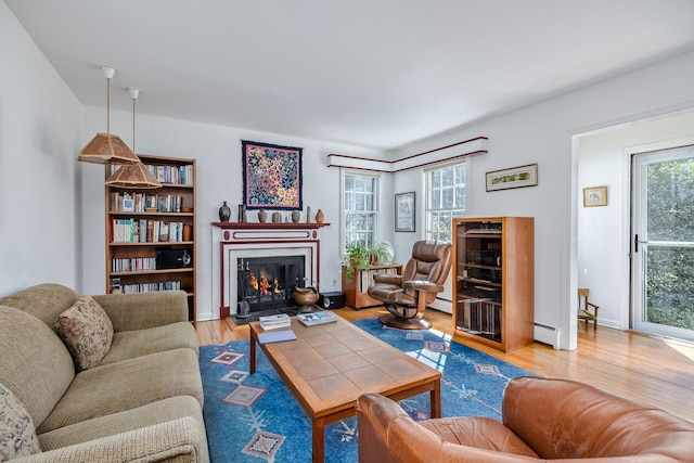 living area featuring baseboard heating, a lit fireplace, and wood finished floors