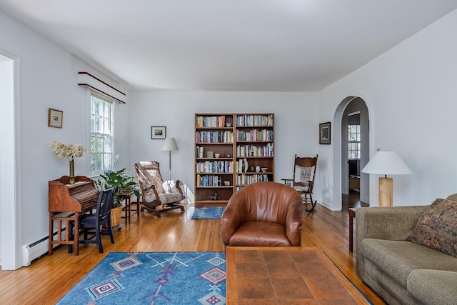 living area featuring arched walkways, a baseboard radiator, and wood finished floors