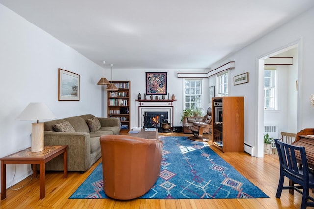 living area with visible vents, a glass covered fireplace, a baseboard heating unit, and hardwood / wood-style flooring