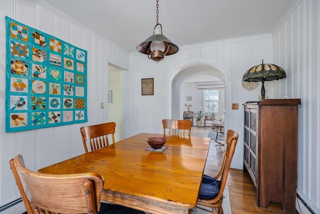 dining area featuring ornamental molding, wood finished floors, a baseboard radiator, baseboard heating, and arched walkways