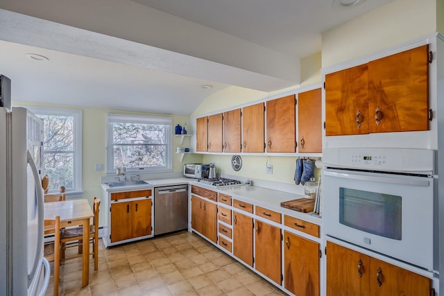 kitchen with lofted ceiling, white appliances, light countertops, brown cabinets, and a sink