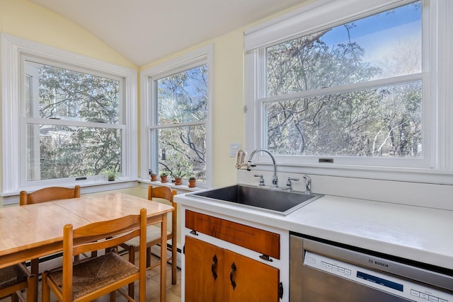kitchen with stainless steel dishwasher, vaulted ceiling, a sink, and light countertops