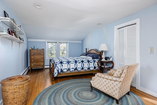 bedroom featuring a baseboard heating unit, vaulted ceiling, wood finished floors, and a closet