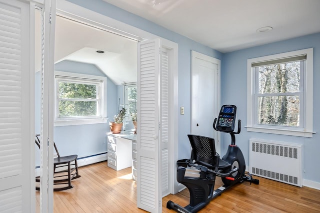 workout area featuring light wood-style floors, radiator, baseboards, and vaulted ceiling