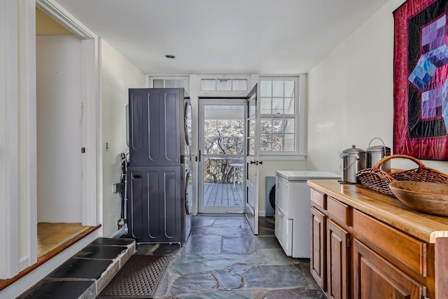 washroom with stone floors, stacked washer / drying machine, plenty of natural light, and a sink
