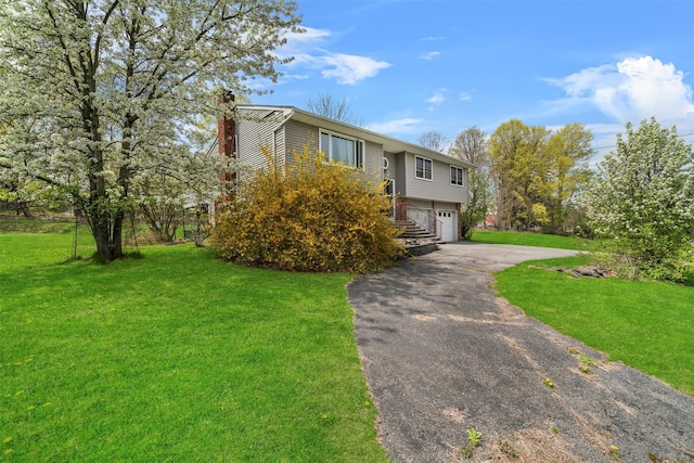 bi-level home featuring a garage, a chimney, driveway, and a front lawn