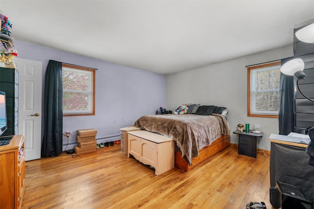 bedroom featuring a baseboard heating unit, multiple windows, baseboard heating, and light wood-type flooring