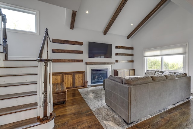 living area with dark wood-style flooring, vaulted ceiling with beams, a glass covered fireplace, recessed lighting, and stairs