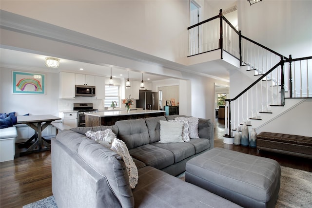 living area featuring stairway, a towering ceiling, visible vents, ornamental molding, and dark wood-style floors