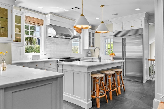 33 Fernwood Rd, Larchmont, NY 10538 - kitchen featuring an island with sink, decorative backsplash, stainless steel appliances, a sink, and wall chimney exhaust hood