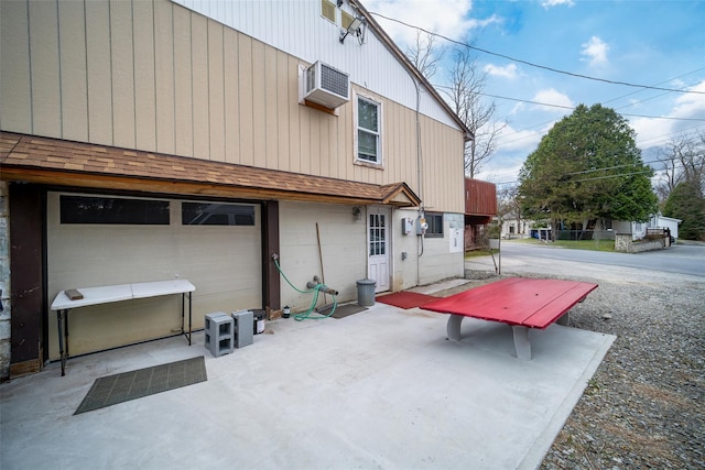 rear view of property with a patio, a wall unit AC, an attached garage, and roof with shingles