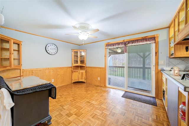 kitchen featuring wood walls, a wainscoted wall, ornamental molding, and a ceiling fan