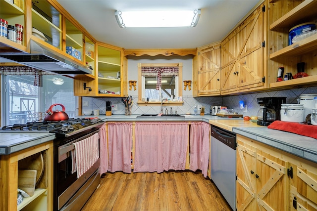 kitchen featuring stainless steel appliances, open shelves, tile counters, light wood finished floors, and a sink