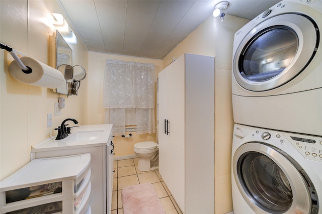 clothes washing area with stacked washing maching and dryer, light tile patterned flooring, laundry area, and a sink
