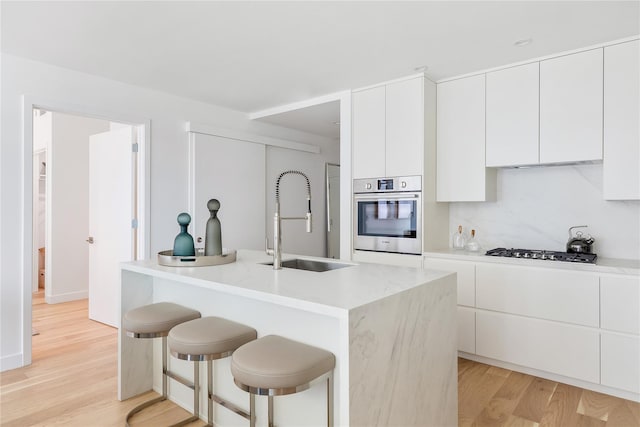 kitchen featuring a sink, white cabinetry, a kitchen breakfast bar, light wood-type flooring, and stainless steel appliances