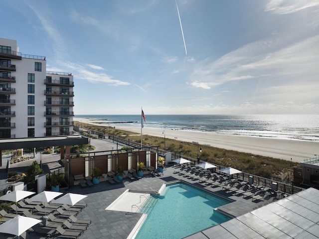 community pool with a water view, a beach view, and a patio