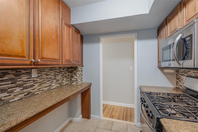 88-25 155th Ave Unit 6L, Howard Beach, NY 11414 - kitchen featuring light tile patterned floors, brown cabinetry, baseboards, stainless steel appliances, and backsplash