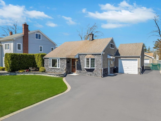 view of front of property featuring fence, a front lawn, stone siding, a garage, and driveway